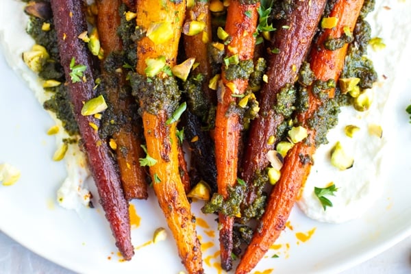 Roasted whole carrots on a white plate with homemade pistachio pesto.