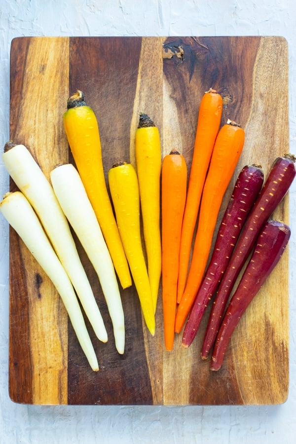 Rainbow carrots that have been peeled and are on a wooden cutting board.