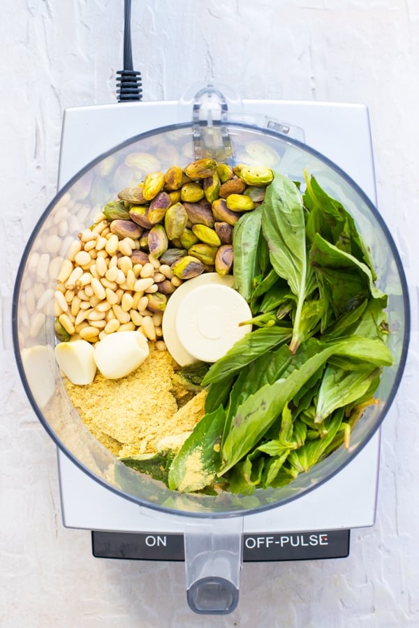 Homemade pistachio pesto ingredients in the bowl of a food processor.