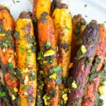 Whole roasted rainbow carrots in a pile on a white plate with pistachios sprinkled around.