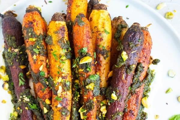 Whole roasted rainbow carrots in a pile on a white plate with pistachios sprinkled around.