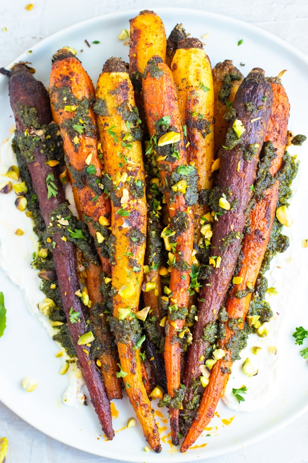 Roasted whole carrots on a white plate on a white background.