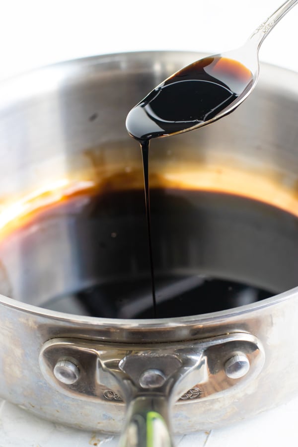 A spoon scooping out a balsamic reduction from a stainless steel saucepan.