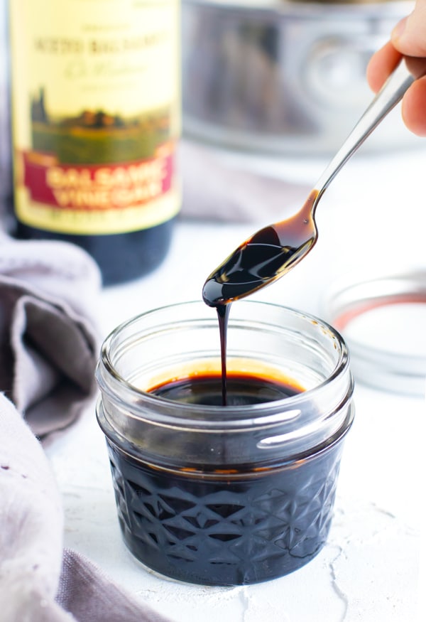 Balsamic vinegar reduction being scooped up by a spoon from a clear mason jar container.