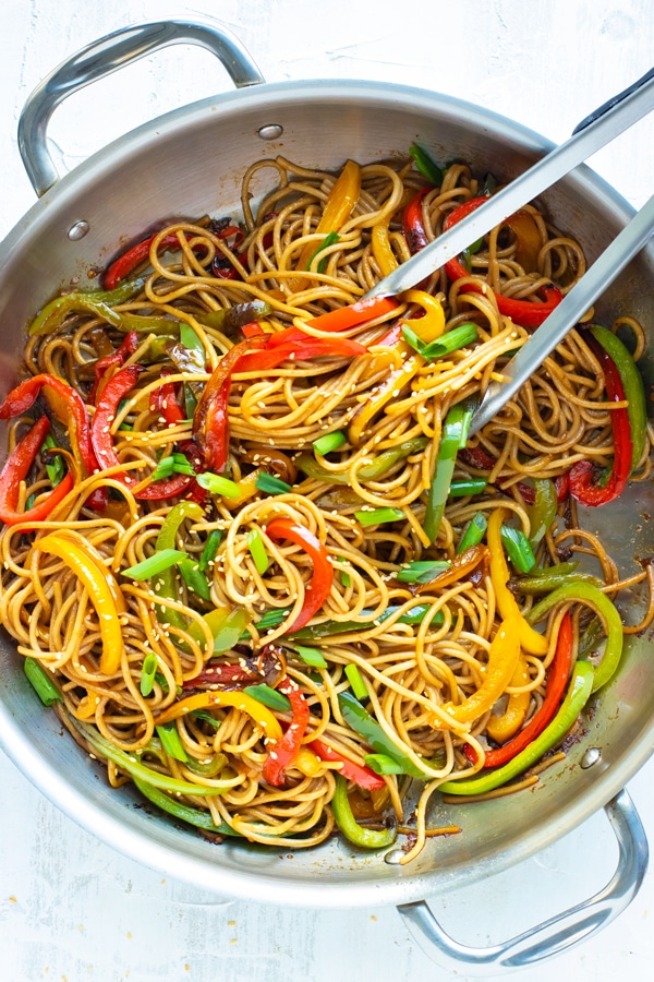 Cold sesame noodles in a wok with red, green, and yellow bell peppers.
