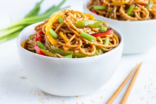 A bowl full of sesame noodles on a white background with chopsticks.