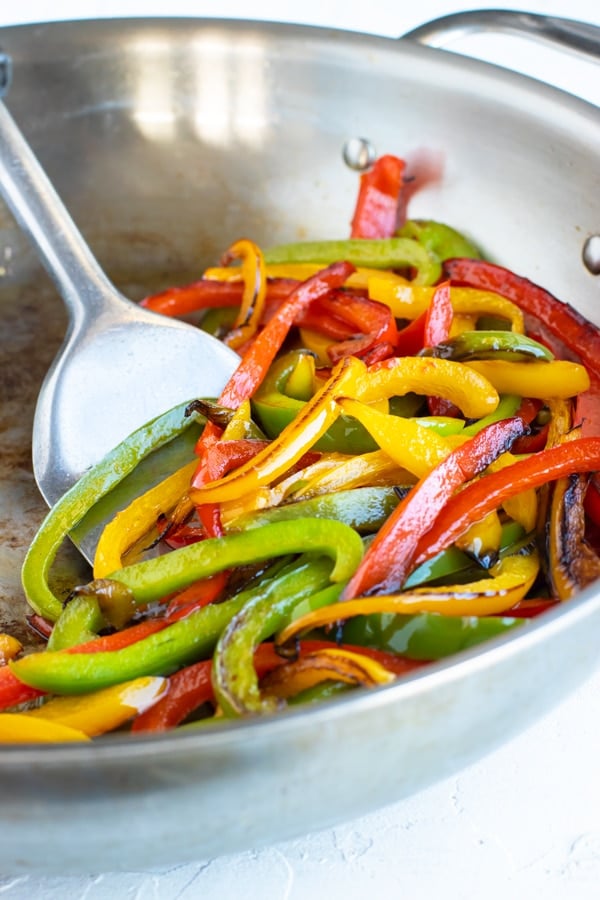 Sauteeing red, green, and yellow bell peppers in a stainless steel skillet.