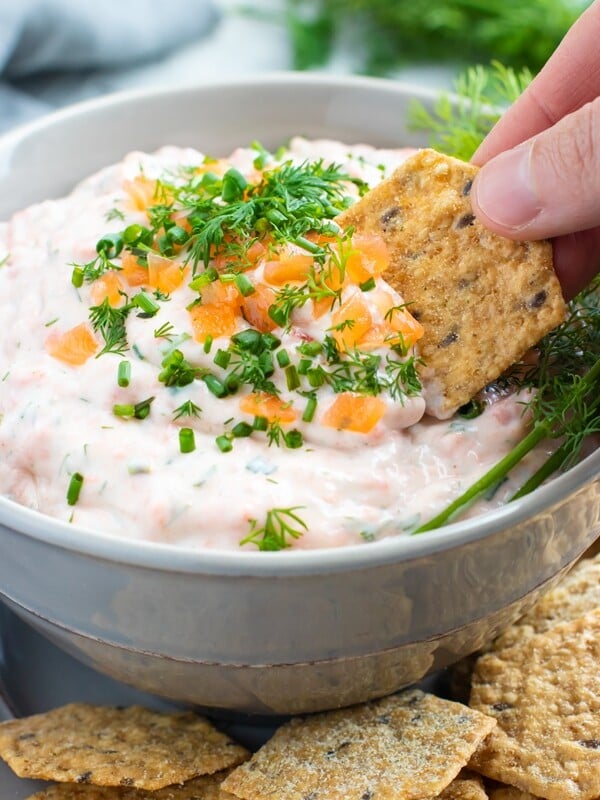 A cracker scooping smoke salmon dip out of a grey bowl.