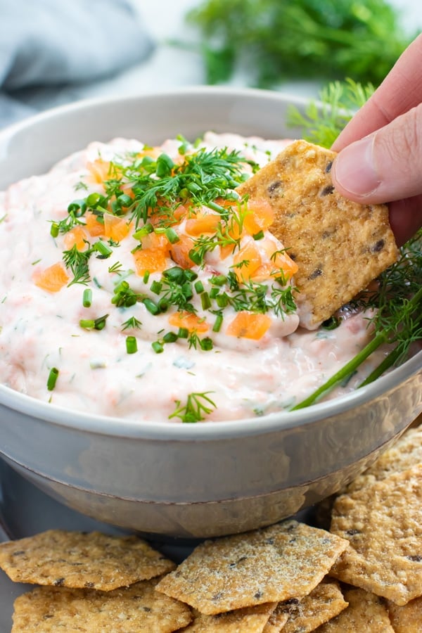 A cracker scooping smoke salmon dip out of a grey bowl.