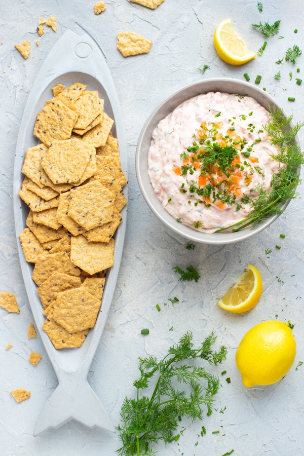 A bowl full of smoked salmon dip next to a plate full of crackers.
