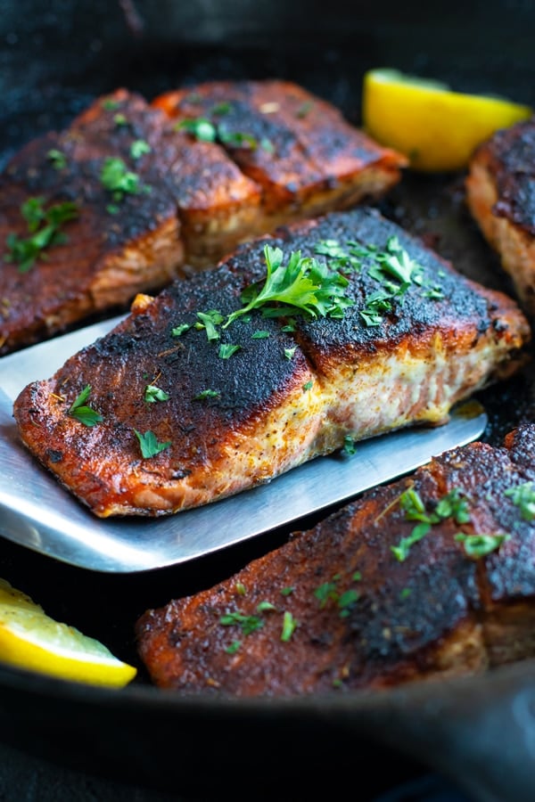 Blackened salmon in a cast iron skillet with lemons and parsley.