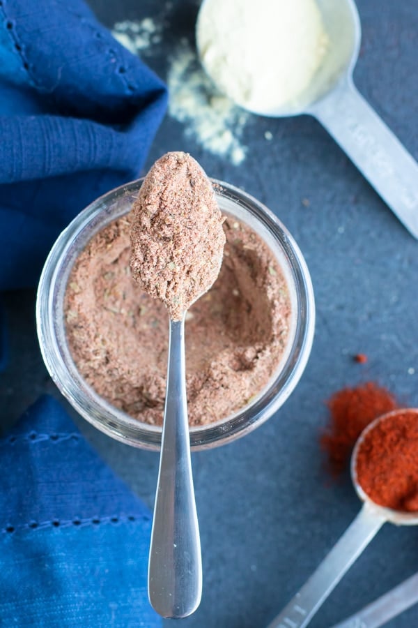 A spoon scooping out homemade blackened seasoning mix from a mason jar next to a teaspoon full of paprika.