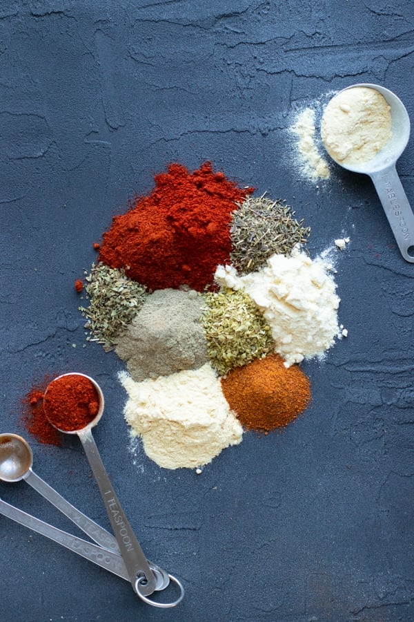 All of the dried spices, dried herbs, and dried peppers on a black board as the ingredients for a homemade Cajun blackened seasoning mix.