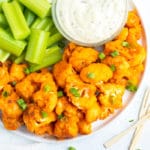 A serving platter full of buffalo cauliflower bites, celery and a bowl of ranch dressing next to toothpicks.