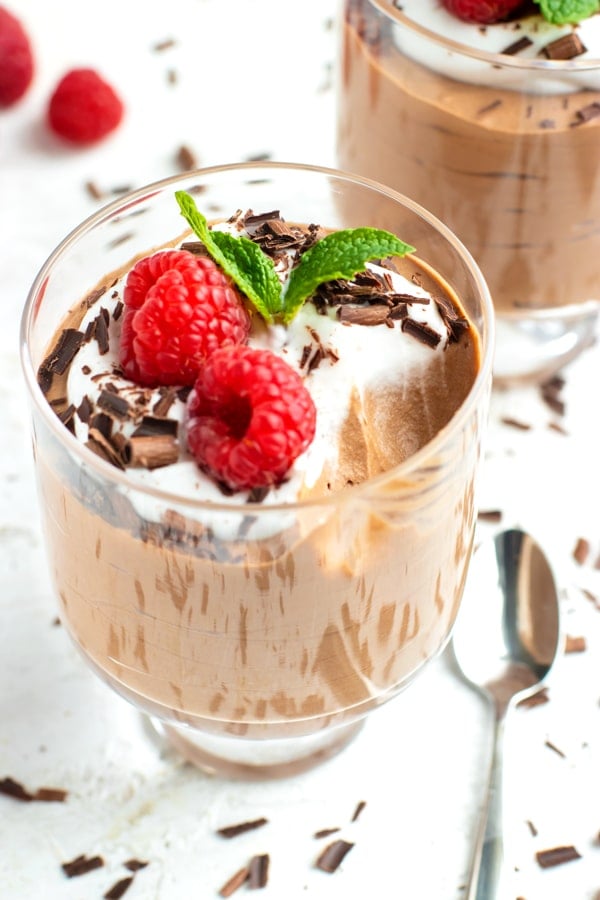 A bite taken out of a parfait glass full of vegan chocolate mousse recipe with a spoon next to it.