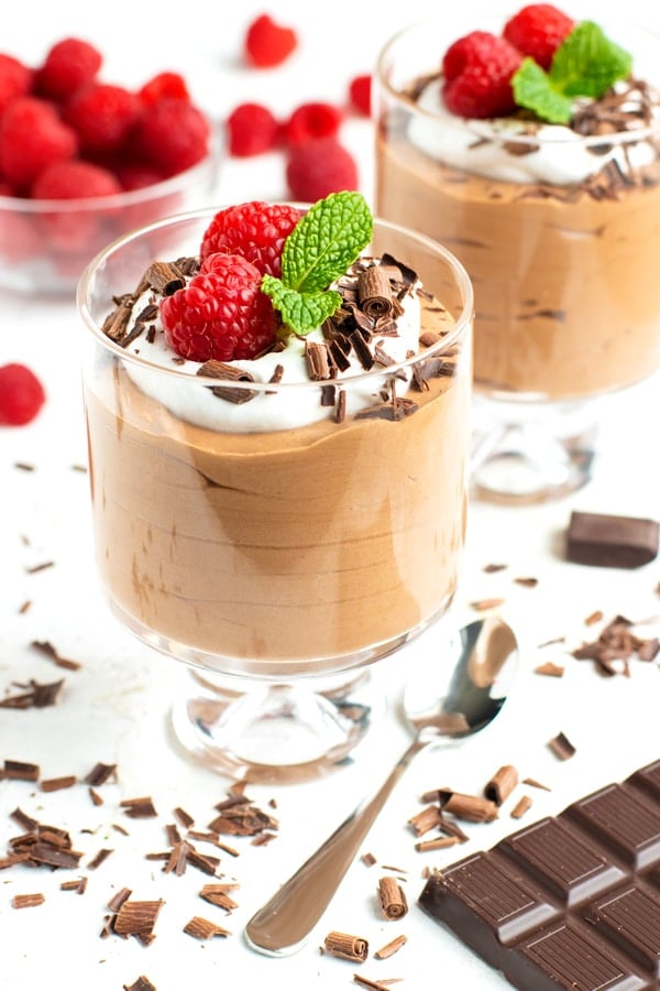 A dessert glass full of chocolate mousse topped with whipped coconut cream and garnished with chocolate curls, raspberries, and mint leaves.