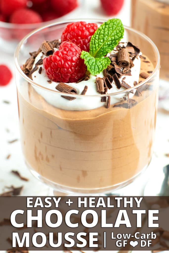 A dessert glass full of chocolate mousse topped with whipped coconut cream and garnished with chocolate curls, raspberries, and mint leaves.