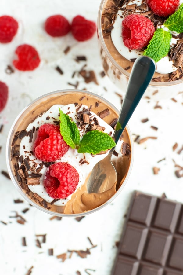 A bite taken out of a parfait glass full of vegan chocolate mousse recipe with a spoon in it.