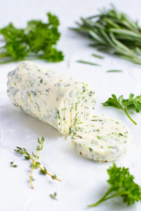 Garlic herb butter on a white table with herbs in the background.