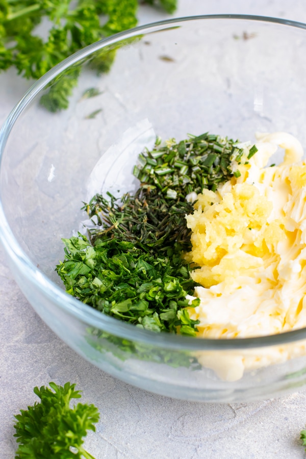 A clear bowl full of butter, garlic, and herbs.