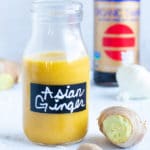 Asian Ginger salad dressing in a clear glass jar with fresh ginger and garlic next to it.