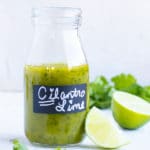 Cilantro lime vinaigrette dressing in a clear glass jar with limes and cilantro next to it.
