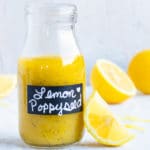 Lemon poppy seed salad dressing in a glass jar with lemon slices next to it.