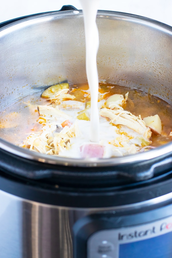 A starch slurry of almond milk and tapioca starch being poured into an Instant Pot to thicken up a chicken vegetable soup recipe.