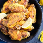 A black bowl full of baked chicken wings with lemon pepper seasoning next to it.