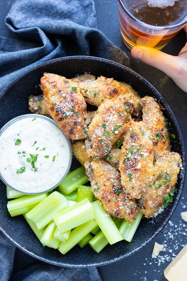 A big bowl of baked chicken wings next to Ranch dressing and celery for a game day party.
