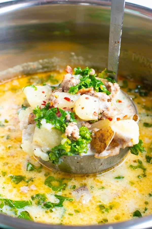 A ladle full of a zuppa toscana recipe with kale, potatoes, and bacon.