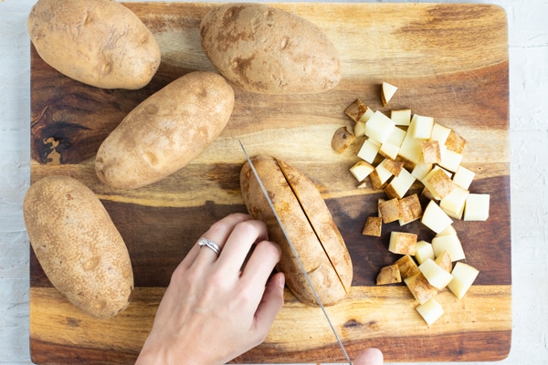 Russet potatoes being cut into 1-inch cubes on a wooden cutting board.