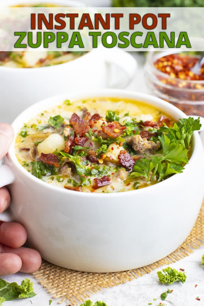 A copycat recipe for Olive Garden zuppa toscana soup in a white bowl with a hand holding it.