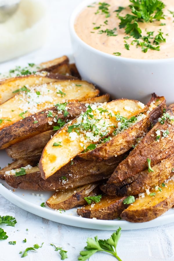A stack of baked potato wedges with Parmesan and parsley sprinkled on top.