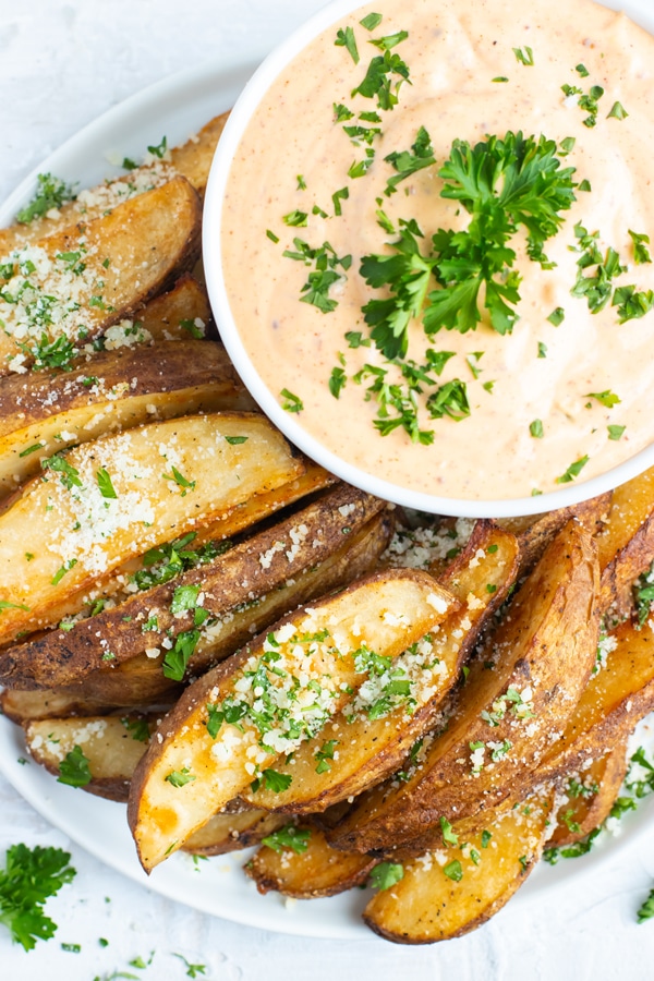 A white plate full of roasted potato wedges and a bowl full of remoulade sauce.