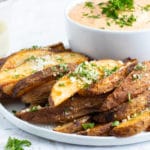 A stack of baked potato wedges with Parmesan and parsley sprinkled on top.