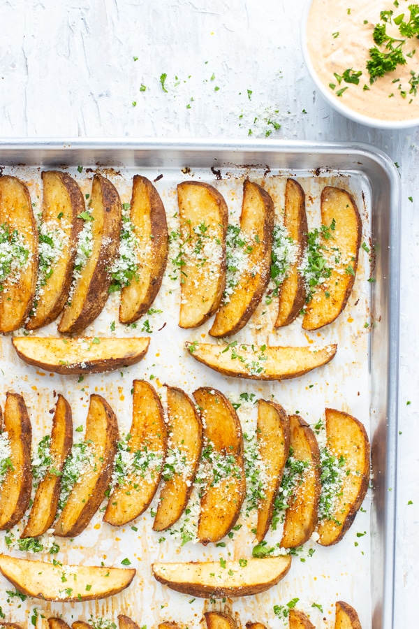 A large baking sheet full of a baked potato wedges recipe with Parmesan cheese and parsley on top.