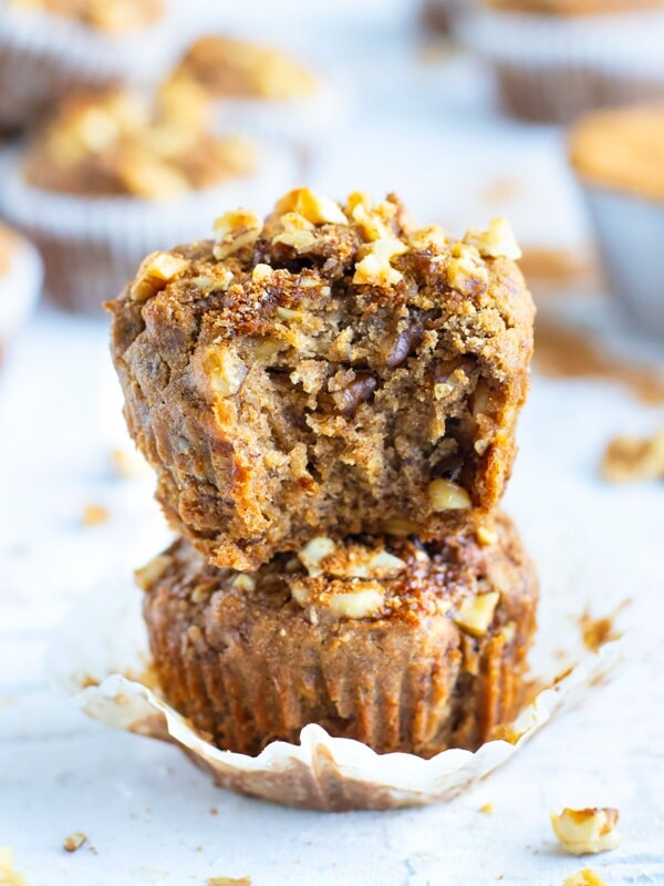 Two healthy banana nut muffins in a stack on a white surface.