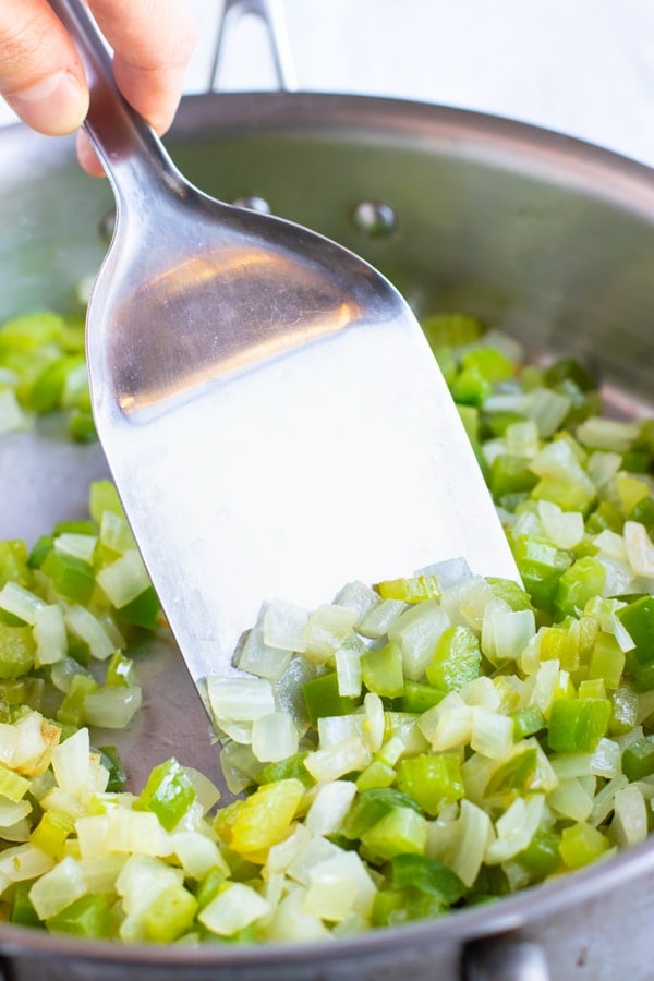 The holy trinity of bell pepper, onion, and celery being sauted in a skillet.