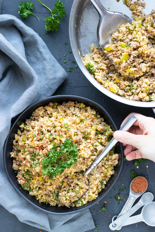 Cauliflower dirty rice in a black bowl with a hand picking up a spoonful of it.
