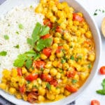 Vegan chickpea curry in a white bowl with basmati rice next to cilantro.