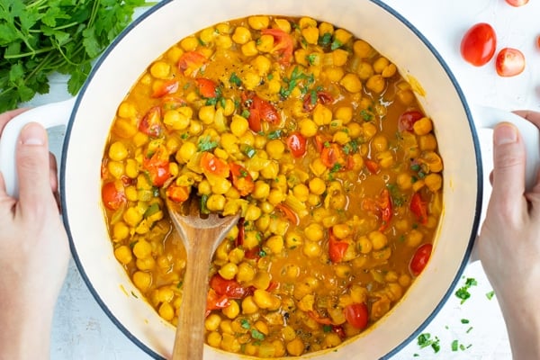 Easy chickpea curry recipe in a white Dutch oven with a wooden spoon.