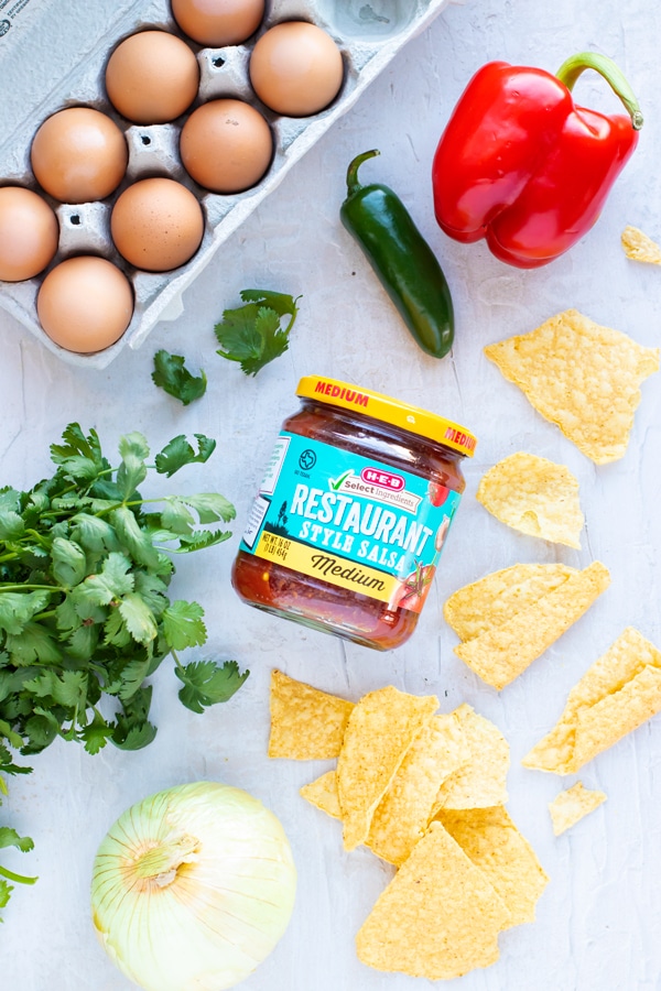 Eggs, bell pepper, jalapeno, corn tortilla chips, onion, and cilantro as the ingredients for a migas recipe.