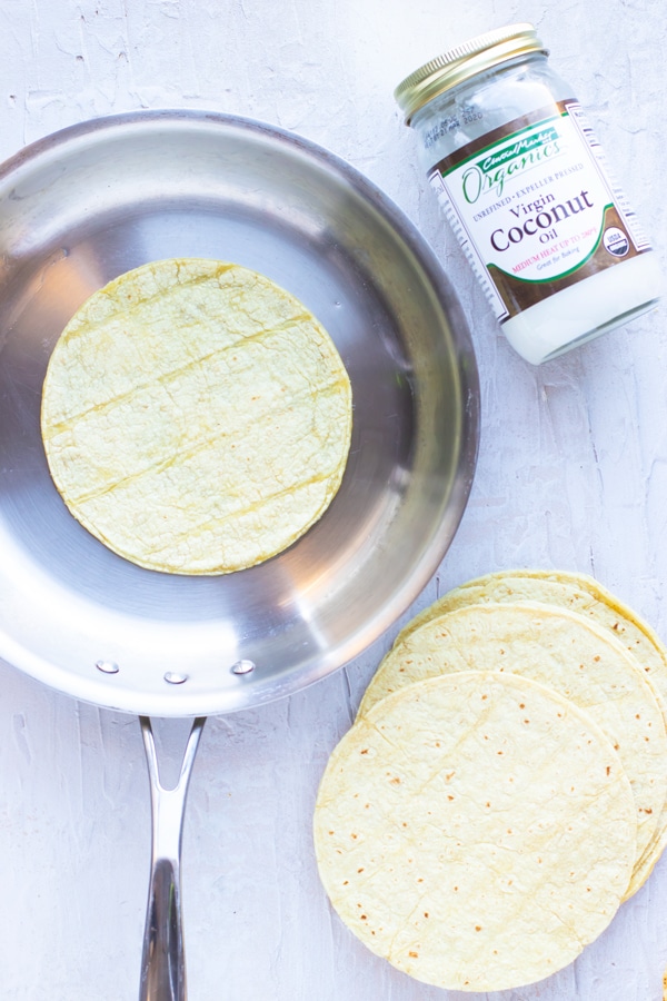 A corn tortilla being heated up with coconut oil in a skillet.