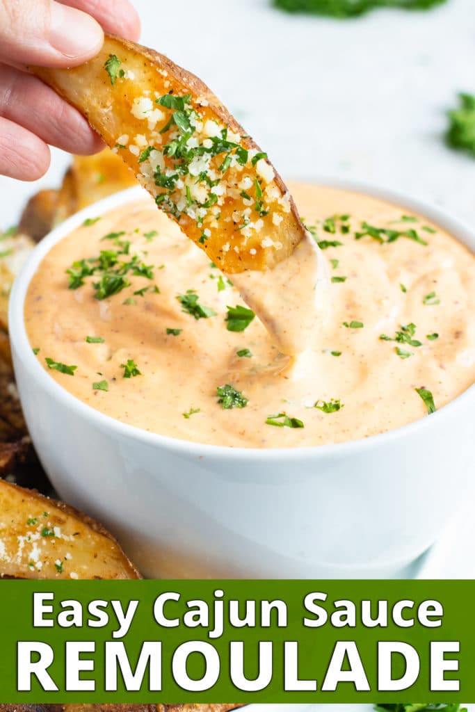 A baked potato wedge being dipped into a bowl full of Cajun remoulade sauce.