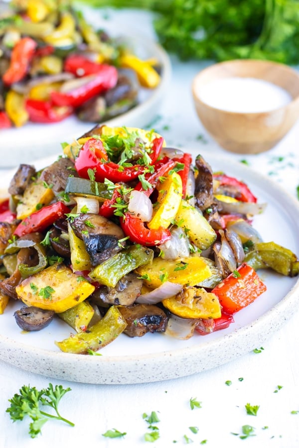 A pile of oven-roasted vegetables on a white plate with another serving in the background.
