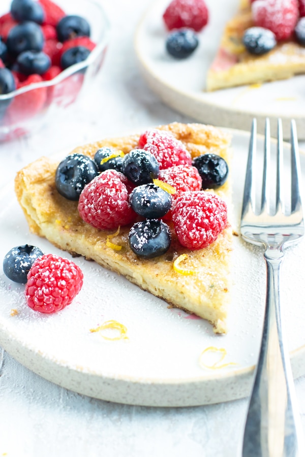 A serving of a Dutch Baby pancake with fresh berries, lemon zest, and powdered sugar on a white plate.