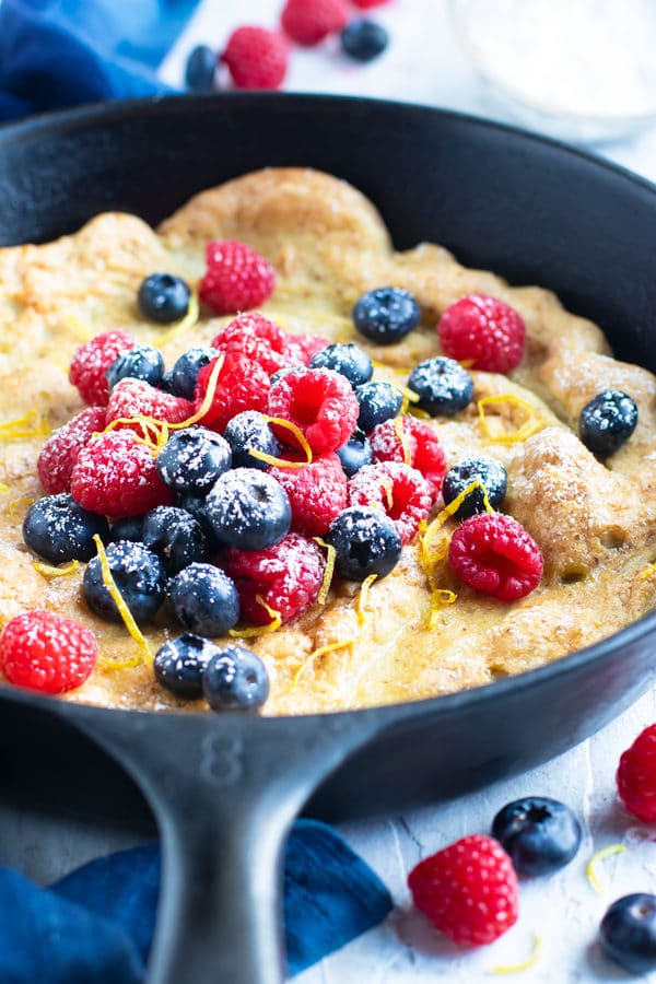 Dutch baby pancake recipe in a cast iron skillet with raspberries and blueberries.