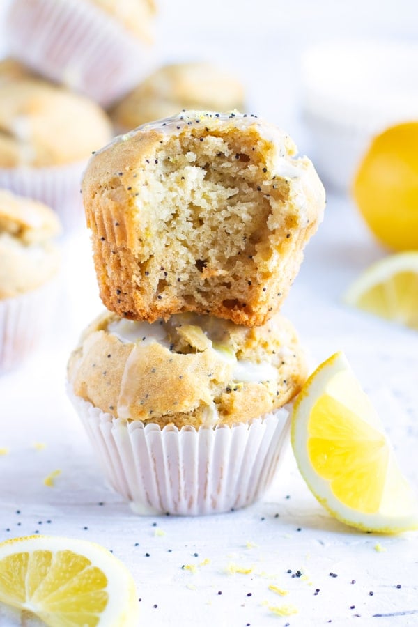 Two lemon poppy seed muffins in a stack with a bite taken out of one next to a lemon wedge.