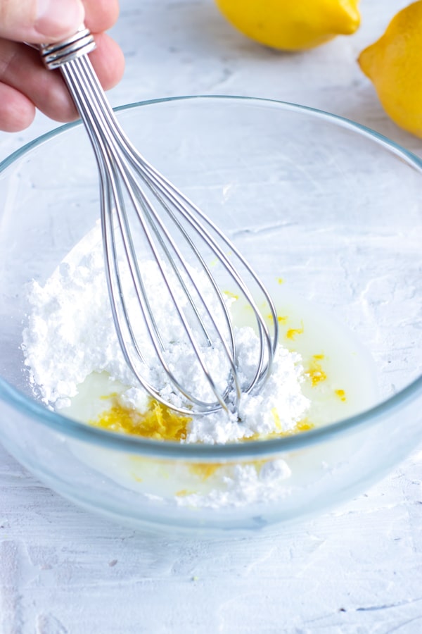 Powdered sugar, milk, and lemon zest being whisked together to make a muffin glaze.